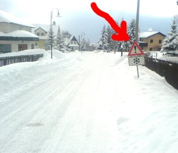 Verschneite Straße mit einem Hinweisschild: Achtung Schneeverwehungen