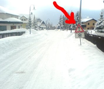 Verschneite Strae mit einem Hinweisschild: Achtung Schneeverwehungen